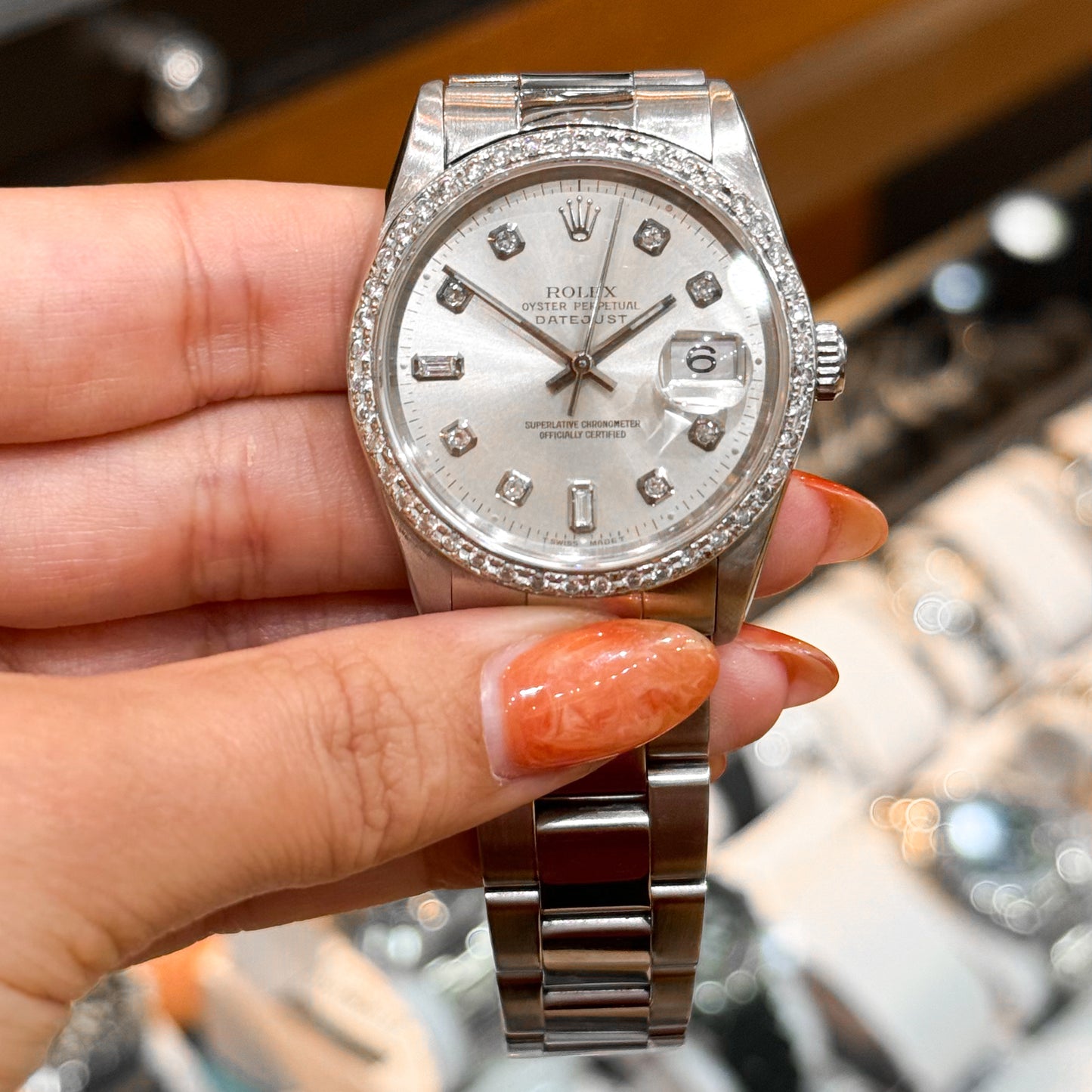 Hand holding a Rolex Datejust with diamond bezel and markers, showcased above a watch tray.