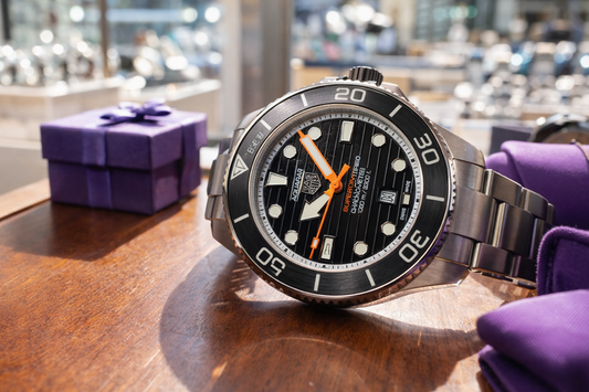 Diver-style wristwatch with black dial and orange seconds hand on a metal bracelet.