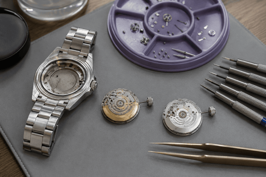 Watch case and two mechanical movements displayed during replacement assessment.