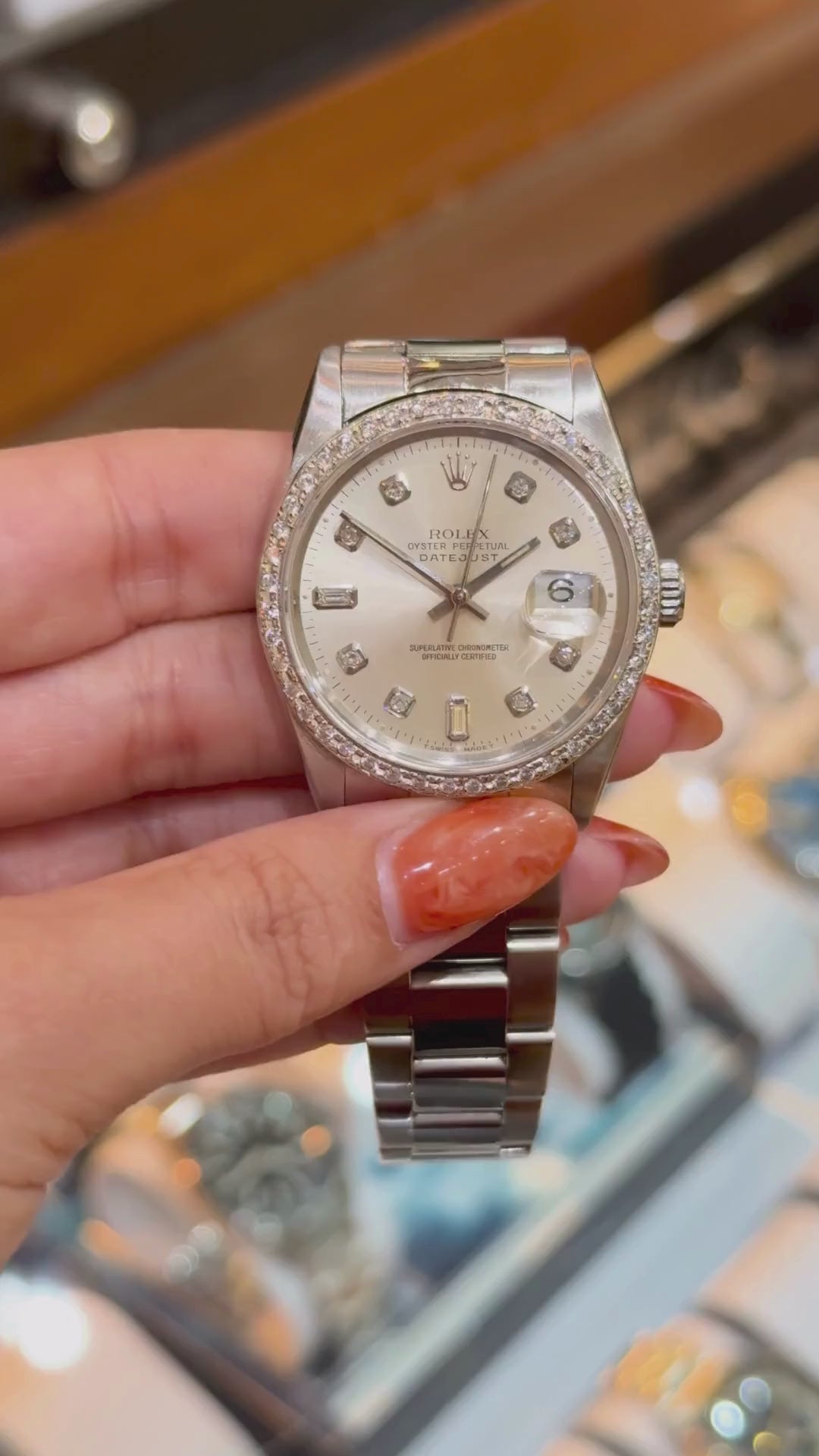 Hand holding a Rolex Datejust with diamond bezel and markers, showcased above a watch tray.